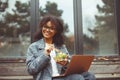 Happy african american woman eating salad, having healthy lunch while resting outdoors with laptop computer Royalty Free Stock Photo