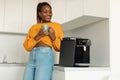 Happy african american woman enjoying fresh aromatic coffee near modern machine in kitchen interior Royalty Free Stock Photo
