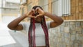 Happy african american woman making lovely heart sign with hands on urban street, radiating joy and confidence Royalty Free Stock Photo