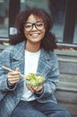 Happy african american woman office worker eating salad outdoors while sitting on bench in park Royalty Free Stock Photo