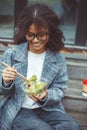 Happy african american woman office worker eating salad outdoors while sitting on bench in park Royalty Free Stock Photo