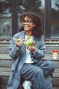 Happy african american woman office worker eating salad outdoors while sitting on bench in park Royalty Free Stock Photo