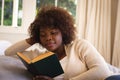 Happy african american woman relaxing in bedroom, lying on bed reading book and smiling Royalty Free Stock Photo