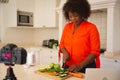 Happy african american woman standing in kitchen preparing food, making vlog using laptop and camera