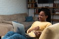 Happy african american woman streaming online movies on a laptop while snacking on popcorn and relaxing on a sofa at home. Black