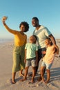 Happy african american woman taking selfie with family from smartphone at beach against blue sky Royalty Free Stock Photo