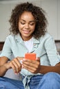 Happy African American woman using phone relaxing on sofa at home. Royalty Free Stock Photo