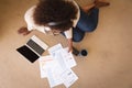 Happy african american woman working in bedroom, sitting floor using laptop and holding paperwork Royalty Free Stock Photo