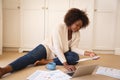 Happy african american woman working in bedroom, sitting on floor using laptop and holding paperwork Royalty Free Stock Photo