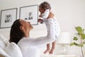 Happy African American young adult mother raising her three month old baby son in the air, smiling at him, close up, side view