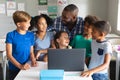 Happy african american young male teacher with multiracial elementary students using laptop Royalty Free Stock Photo