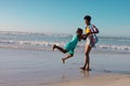 Happy african american young woman spinning playful daughter at shore against sea and clear sky