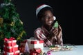 Happy African boy smile and holding Christmas tree shape cookie in hand near little Christmas tree on black background Royalty Free Stock Photo