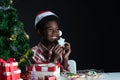 Happy African boy smile and holding snowflake shape cookie in hand near little Christmas tree on black background Royalty Free Stock Photo