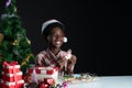 Happy African boy smile and holding snowman shape cookie in hand near little Christmas tree on black background Royalty Free Stock Photo