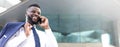 Happy african businessman holding his phone while standing near the building and looking straight ahead Royalty Free Stock Photo