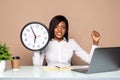 Happy african american businesswoman sitting at the table with clock time finish of work and laptop in office over gray background