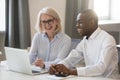 Happy african and caucasian colleagues talking in office at laptop Royalty Free Stock Photo