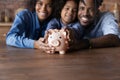 Happy African couple and little daughter posing indoor with piggybank Royalty Free Stock Photo