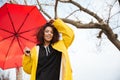 Happy african curly young lady wearing yellow coat with umbrella