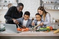 Happy african cute little sons and their young parents having online cooking class on laptop Royalty Free Stock Photo