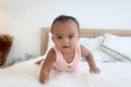 Happy African cute toddle baby infant girl crawling on white bed in bedroom. Portrait of adorable little kid child at home, happy Royalty Free Stock Photo