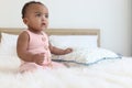 Happy African cute toddle baby infant girl sitting on white bed in bedroom. Portrait of adorable little kid child at home, happy Royalty Free Stock Photo