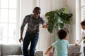 Happy african dad laughing running in living room catching kids