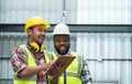 Happy African engineer and Asian foreman in safety hat working together at warehouse while listing on clipboard to discuss, Royalty Free Stock Photo
