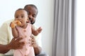 Happy African family, father holding his little cute toddle baby infant daughter girl while sitting on white bed in bedroom. Dad Royalty Free Stock Photo
