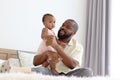 Happy African family, father holding his little cute toddle baby infant daughter girl while sitting on white bed in bedroom. Dad Royalty Free Stock Photo