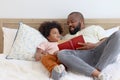 Happy African family, father and son spending time together, young boy with black curly hair and dad reading a book together while Royalty Free Stock Photo