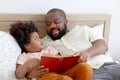 Happy African family, father and son spending time together, young boy with black curly hair and dad reading a book together while Royalty Free Stock Photo