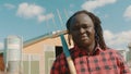 Happy african farmer holding fork over the soulder and nodding his head in front of the silo system