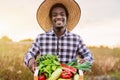 Happy African farmer working in the countryside holding a wood box with vegetables