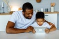 Happy african father and his little son using laptop at home together, watching movies online or browsing internet