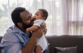 Happy African father man sitting holding and kissing newborn son baby on a sofa in the living room at home Royalty Free Stock Photo