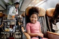 Happy African girl child, kid passenger sitting in comfortable seat inside airplane during female air hostess pushing cart on Royalty Free Stock Photo