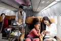 Happy African girl kid and woman passenger look at mobile phone during sit in comfortable seat inside airplane, female cabin crew Royalty Free Stock Photo