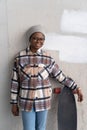 Happy african girl with longboard over concrete wall smiling wear casual clothes, glasses, earnings Royalty Free Stock Photo