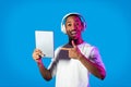 Happy african guy using digital pad, wireless headphones on blue Royalty Free Stock Photo