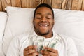 Happy African Man Holding Money Counting Cash Lying In Bed