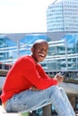 Happy african man sitting outside using phone and laughing Royalty Free Stock Photo