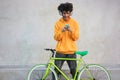 Happy african millennial boy with bike listening music with headphones outdoors - Focus on face app