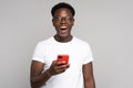 Happy African millennial man in glasses wear white t-shirt holding mobile phone isolated on studio