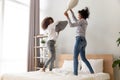 Happy african mom and teen having pillow fight on bed