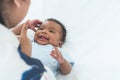 Happy African Nigerian newborn baby lying on white bed at home with mother talking and playing. Innocence infant with curly hair Royalty Free Stock Photo