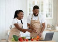 Happy African Spouses Using Laptop Computer While Cooking In Kitchen, Searching Recipe Royalty Free Stock Photo