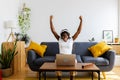 Happy african student woman sitting on sofa with laptop and celebrating success Royalty Free Stock Photo