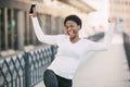 Happy African woman listens to music with headphones and dances outdoors on a city street Royalty Free Stock Photo